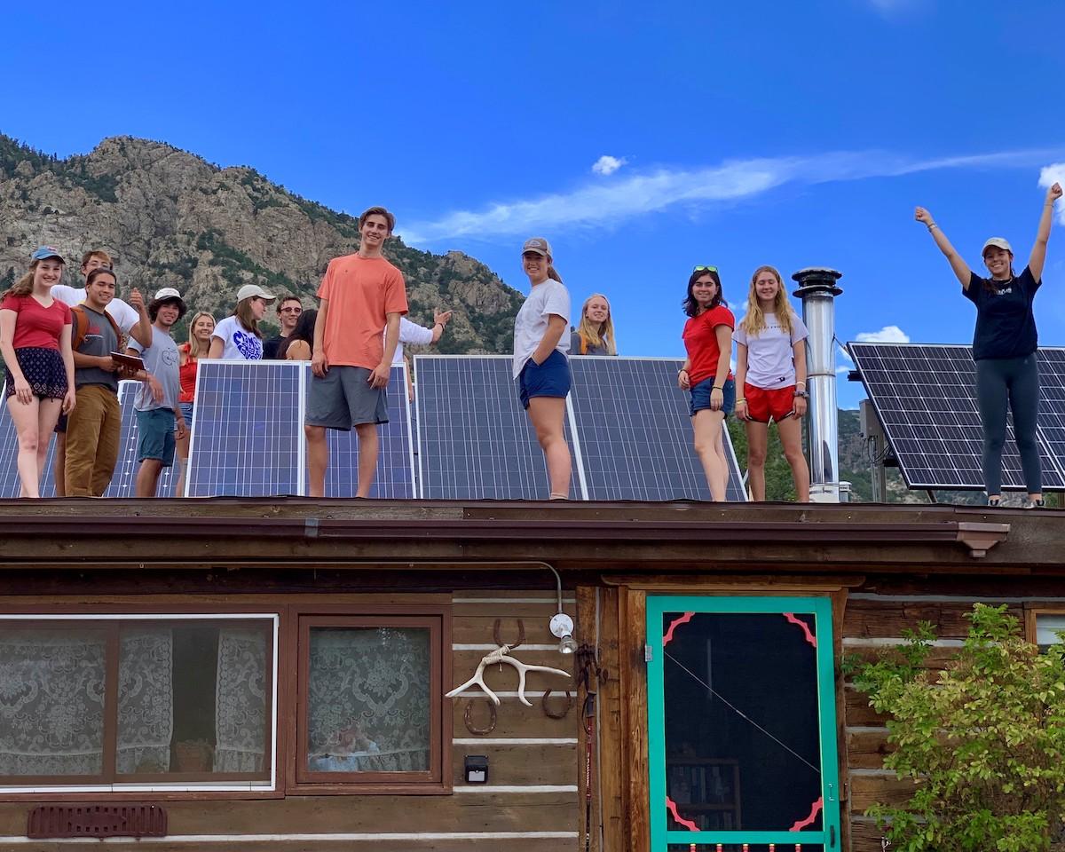 college students on top of a roof next to newly installed solar panels and celebrating